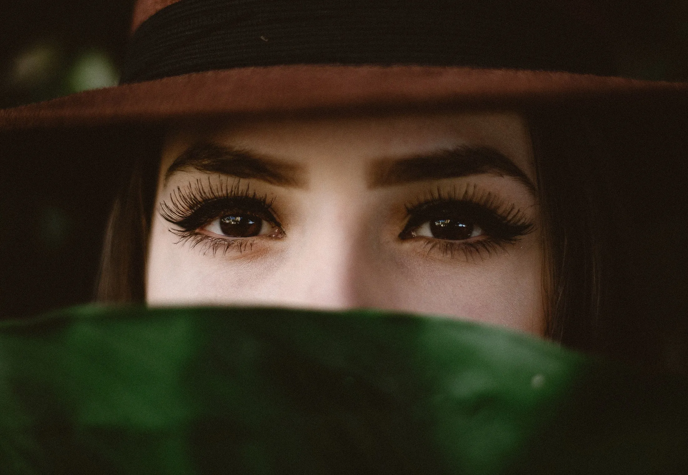 Ojos maquillados con pestañas marcadas, mirada bajo un sombrero
