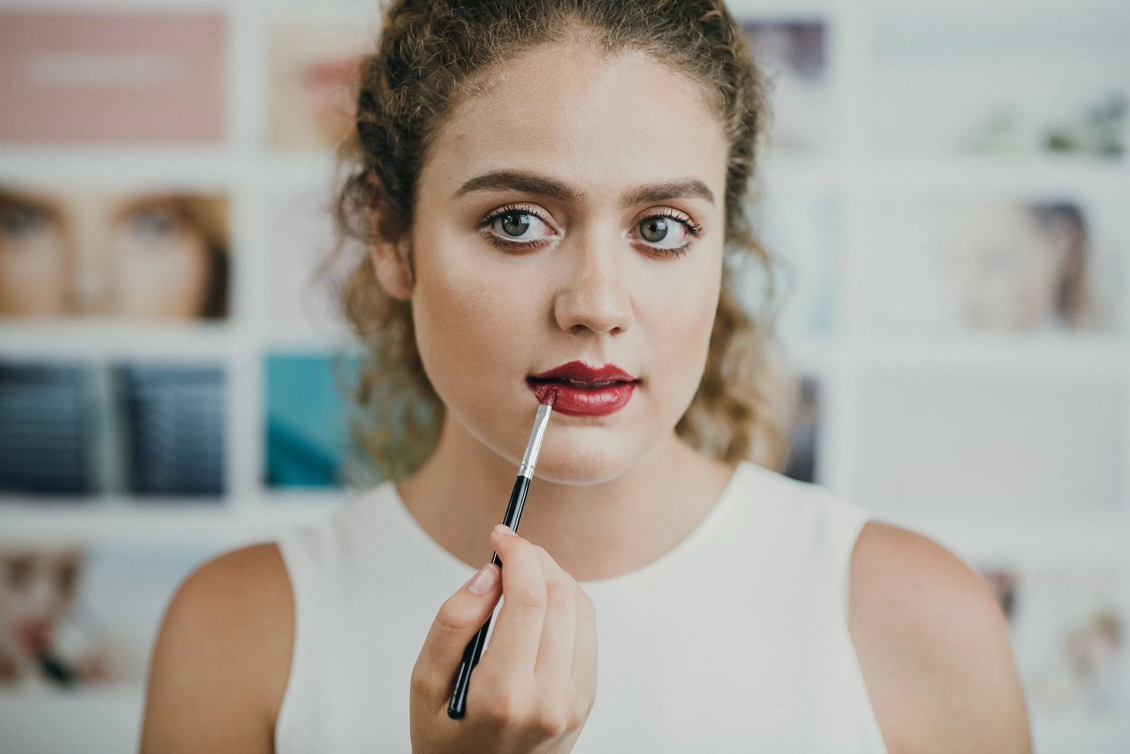Modelo con maquillaje natural sosteniendo un pincel de labios, panel de referencias de fondo
